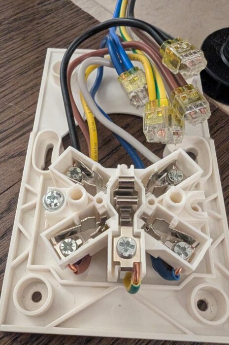 Närbild av en Perilexkontakt med fyra inkopplade färgade kablar på en vit platta.