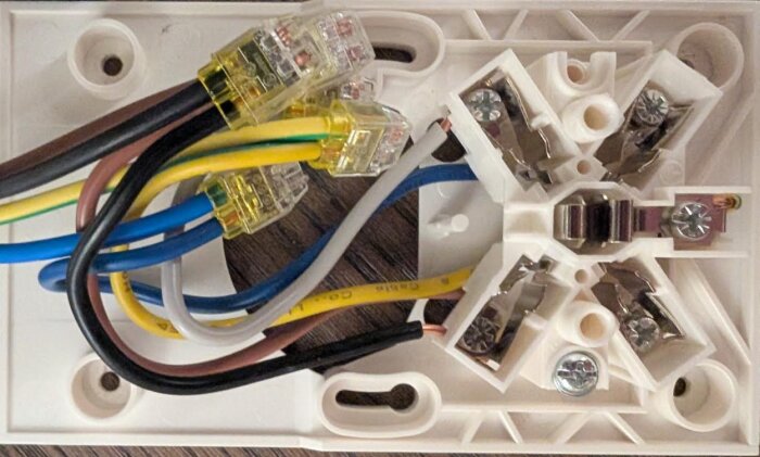 Närbild på en öppen Perilexkontakt med flera kopplade kablar i olika färger, inklusive blå, brun, gul och grön.