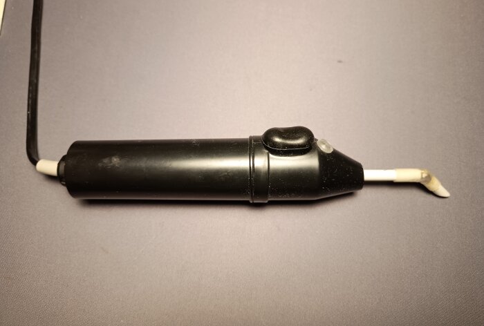 Svart defluxer eller avmagnetiserare med svart handtag och spetsig vit tipp placerad på ett bord.