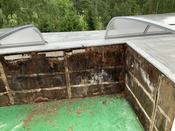 Ruttna och skadade plywoodskivor i en äldre poolkonstruktion, omgiven av stukat stenläggning och grön poolbotten.