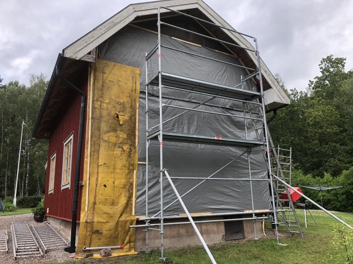 Ställning och presenning skyddar gavel på rött hus under blåsigt väder.
