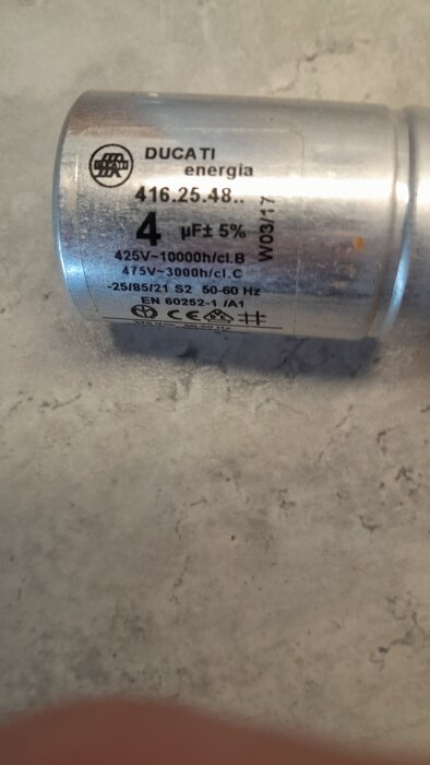 Stor kondensator på 4μF från Ducati energi, märkning och specifikationer synliga, placerad på köksbänk som tänkbar orsak till fläktproblem.