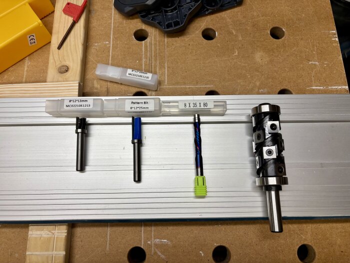 Fyra olika mallfräsar med förpackningar placerade på en arbetsytan av trä och metall, inklusive en stor spiralfräs till höger.