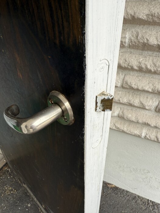 Närbild av en utomhusdörr med ett metallhandtag; dörrkarmen är vitmålad och visar ett urtag för eventuellt lås.