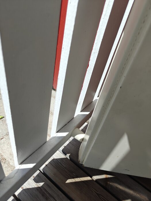 Dörrstopp i trä hindrar en vit dörr från att öppnas förbi ett räcke, men vinden kan orsaka att dörren glider förbi.