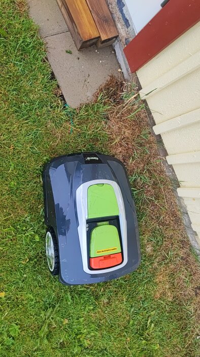 Gräsklippare vid kanten av en gräsmatta och en byggnad, stannad intill träplankor.