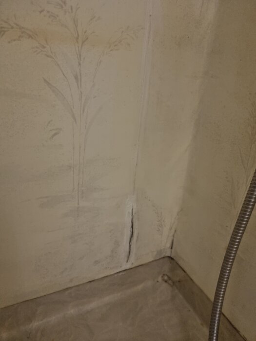 Spricka i våtrumsmatta med tätad silikon i duschhörna med duschslang synlig.