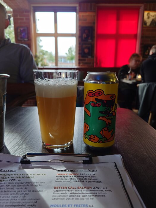 Ölglas och färgglad burk på bord i restaurangmiljö med matsedel i förgrunden.