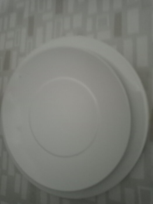 Två vita tallrikar staplade på ett bord med grått geometriskt mönster.