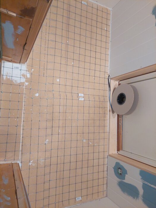 Armeringsnät fastskruvat på golv, förberett för golvvärmekabel i ett rum under renovering. Målad vägg och material syns intill.