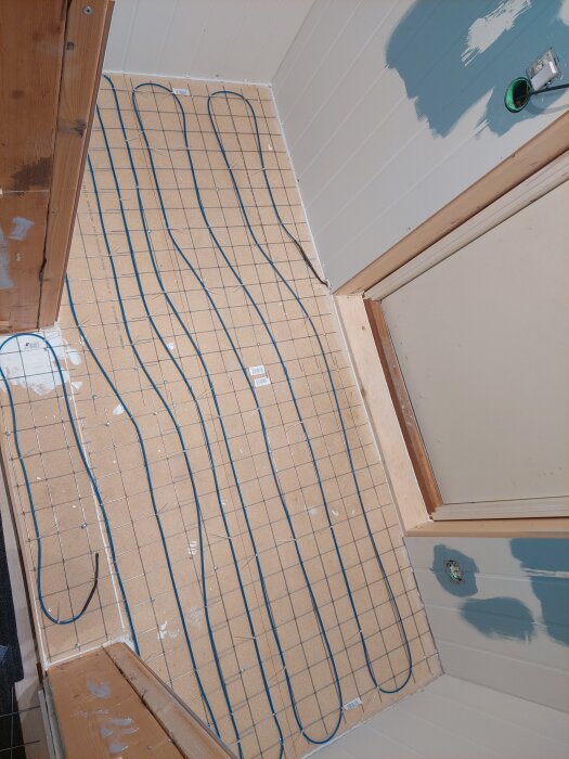 Golvet med utlagda armeringsnät och golvvärmekablar, fixerat med buntband, i ett pågående renoveringsprojekt.