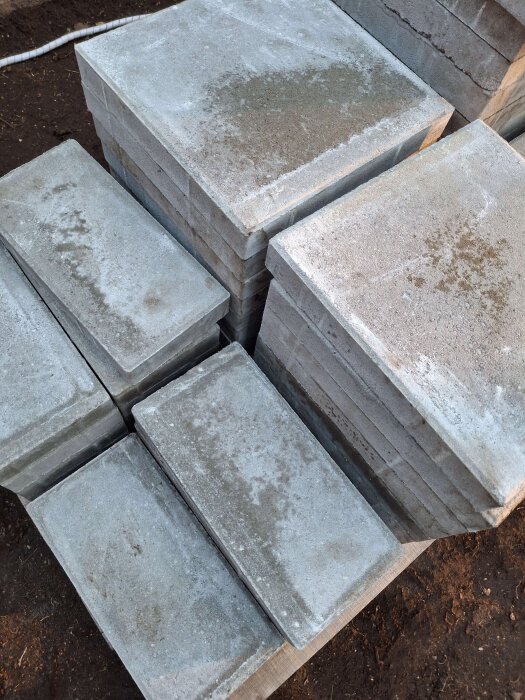 Staplade betongplattor i olika storlekar på en jordig yta, avsedda för att bygga grunden till ett växthus.