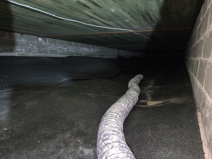 Flexibelt rör installerat i krypgrund med plastöverdrag vid sidan av betongvägg.