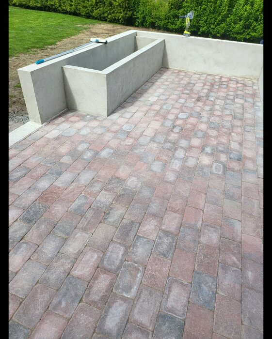 Sandiga plattor efter fogning i ett växthus under konstruktion med en betongvägg och en kvast på marken.