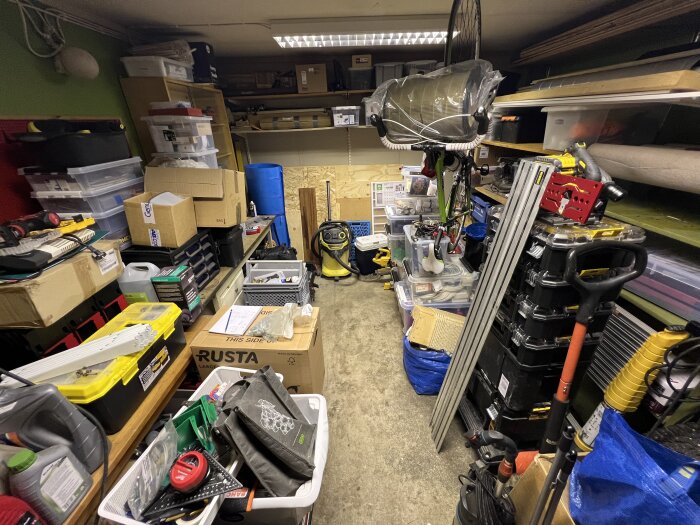Rörigt garage fullt med verktyg, lådor och diverse föremål, med en cykel upphängd i taket och trånga ytor för en bil.