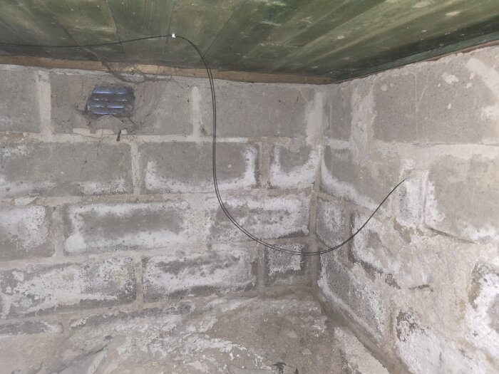 Fiberkabel hänger från taket i ett hörn av en krypgrund med synliga betongblockväggar.