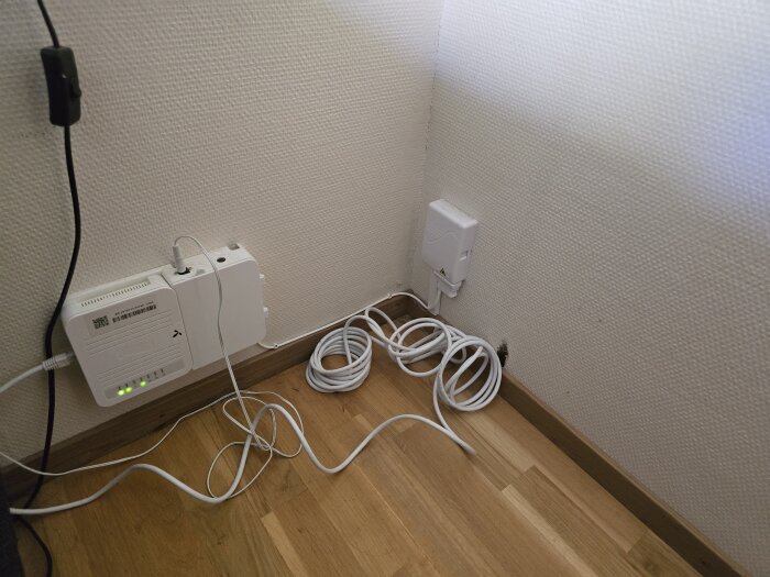 Stamkabel och router installerade på golv med kablar i en hörna av rummet.