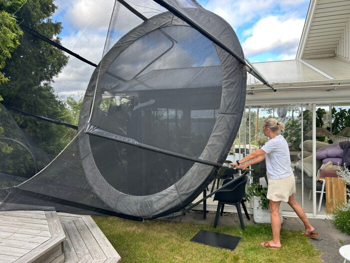 Kvinna håller i en omkullvält studsmatta nära ett hus under en storm.