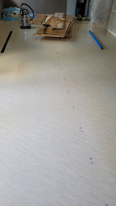 En golvyta med plastmatta syns, omgiven av verktyg och material.