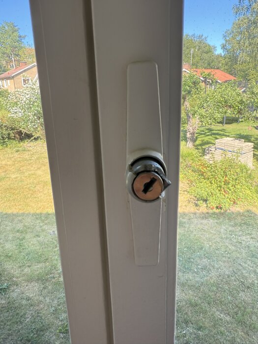 Gammalt fönsterhandtag i vitt och metall på ett fönster, delvis trasigt och utan synliga skruvhål, från 50-talet.