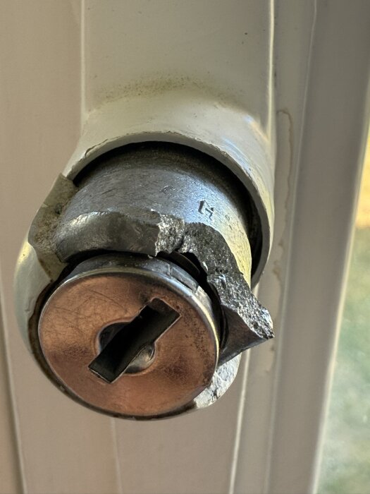 Förstört gammalt fönsterhandtag i metall från 50-talet, brutet i två delar utan synliga skruvhål, monterat på en vit fönsterram.