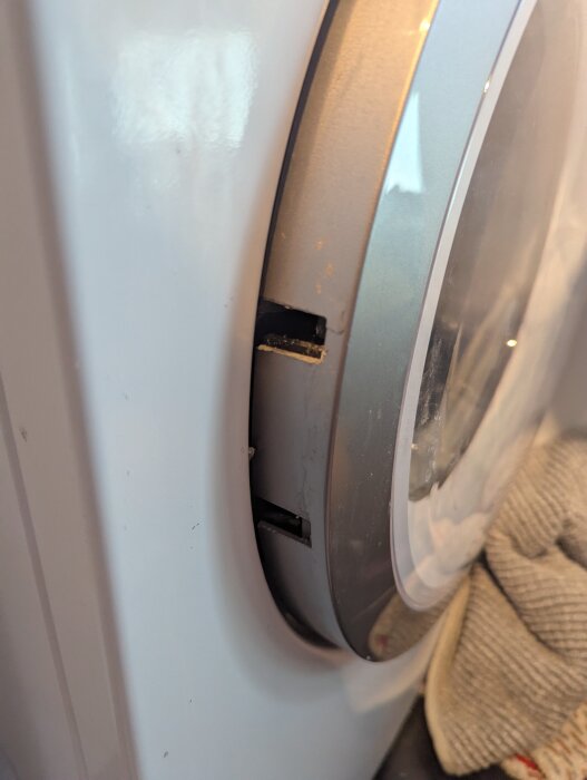 Närbild på en tvättmaskinslucka med ett trasigt gångjärn; luckan på en Bosch tvättmaskin har hoppat ur ramen.