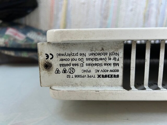 Etikett och ventilation på sidan av ett fläktkonvektorelement, text och symboler synliga. Elementet är monterat nära en vägg.