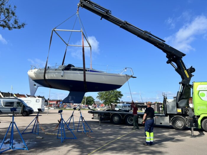 Båt lyfts med kran inför sjösättning, personer övervakar processen på en hamnplats.