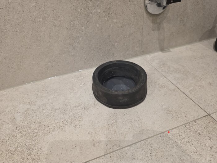 Golv i badrum med svart röranslutningsmanschett för toalett, cirka 40mm hög, monterad i kakelgolv nära vägg.