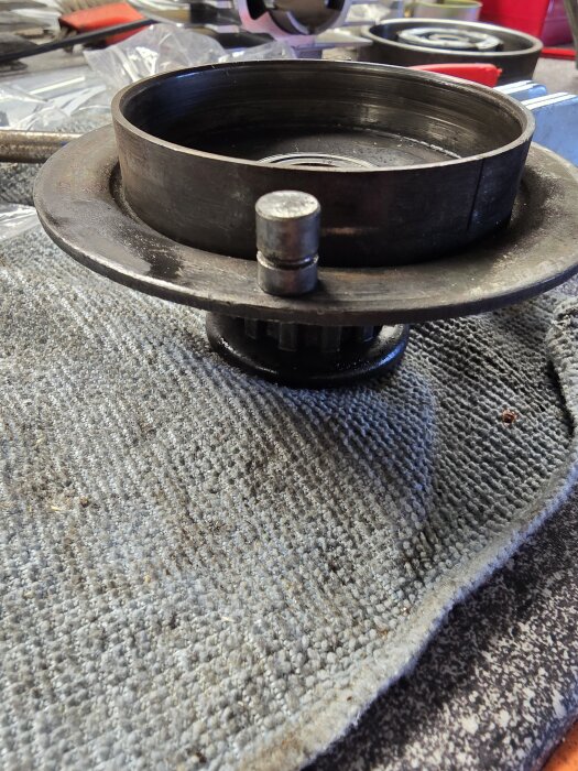 Gammal metallkomponent på en verkstadsmatta, med fokus på enhetens kanter och yta, delvis upphöjd.