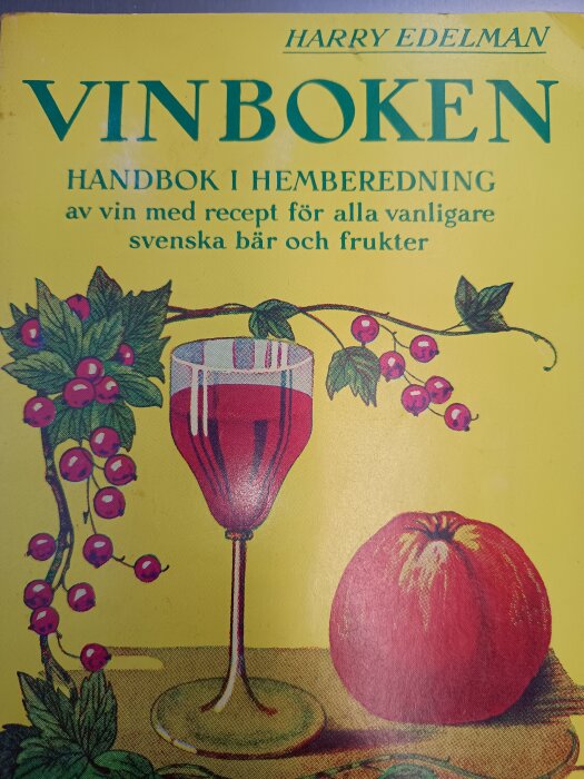 Omslaget till "Vinboken" av Harry Edelman med illustration av ett glas rött vin, vindruvor och äpple mot gul bakgrund.