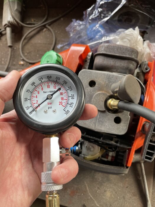Man håller en tryckmätare vid en motor, visar låg kompression, vilket kan förklara varför maskinen inte startar.