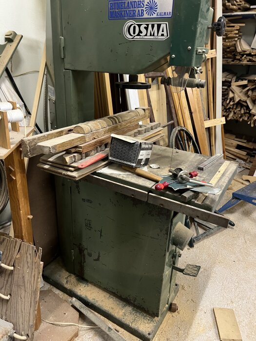 Bandsåg i en verkstad med träbitar och verktyg på arbetsytan.