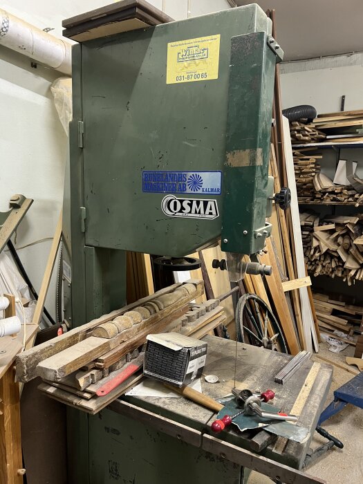 Bandsåg i verkstad omgiven av trä och verktyg.