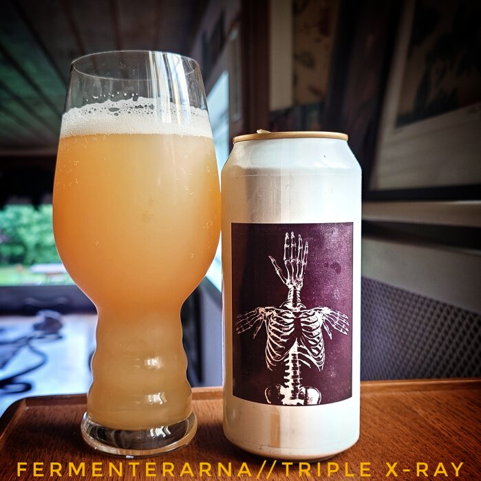 Glas med grumlig dryck och en ölburk med skelettmotiv från Fermenterarna, märkt "Triple X-Ray", står på ett bord.
