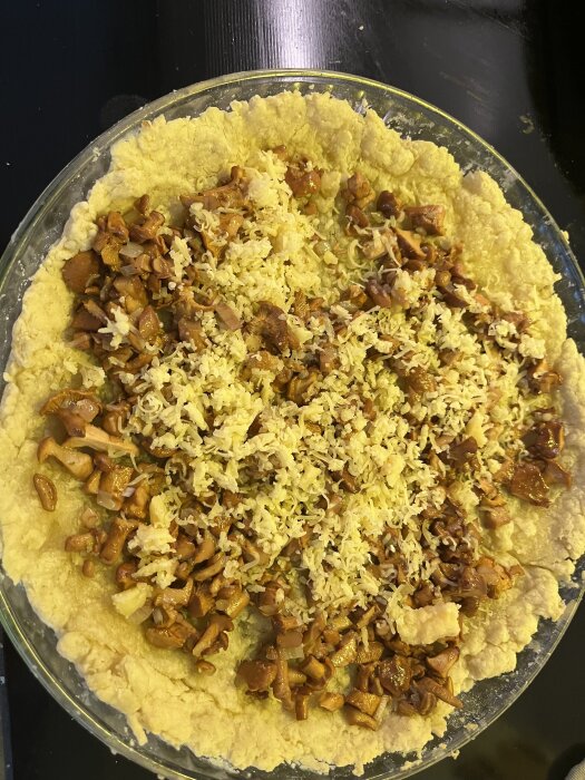 Kantarellpaj med riven Västerbottenost i ett pajskal på en svart bakgrund.