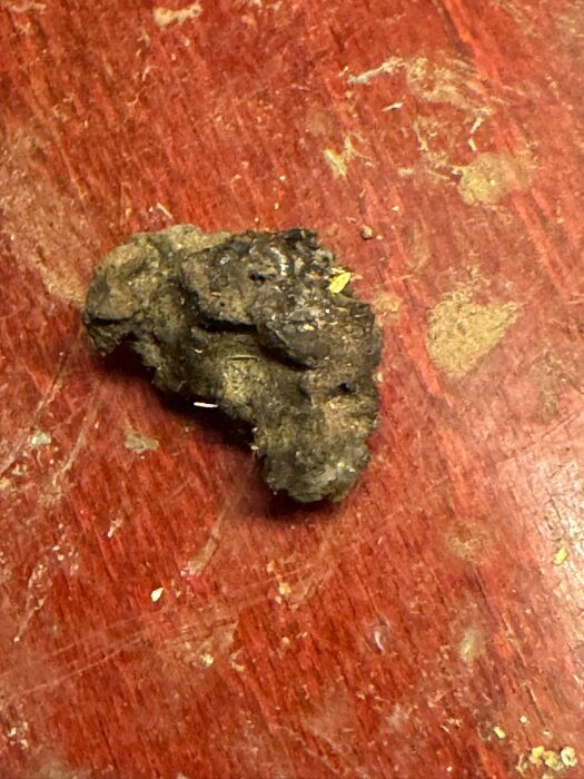 Fragment av stenliknande material med ojämn yta och mörk färg ligger på brunröd träyta, använt som fyllnadsmaterial i gammalt hus.
