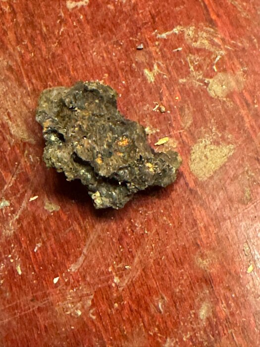 Stenbit på röd träyta, ser ut som vulkanisk sten, del av fyllnadsmaterial i trossbotten av ett gammalt hus, storlek varierar mellan 1-8 cm.