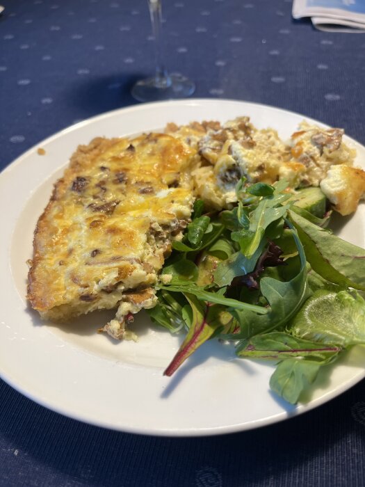 Tallrik med en färdig gratängbit och en sallad placerad på ett mörkt bord.