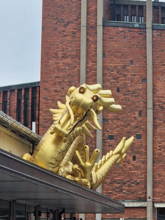 Uppblåsbar gulddrake sitter på ett tak framför en röd tegelvägg.