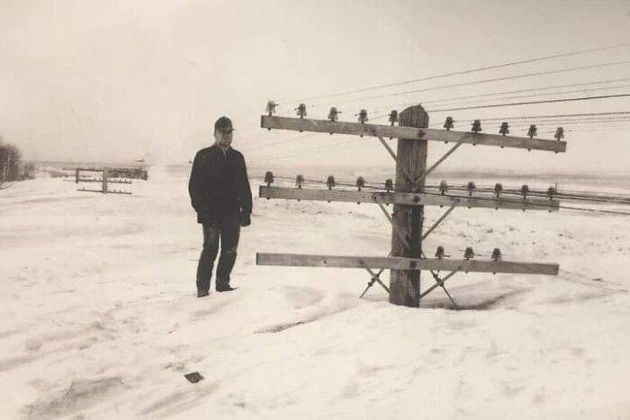 Man står bredvid en nedfallen telefonstolpe i ett snötäckt landskap.