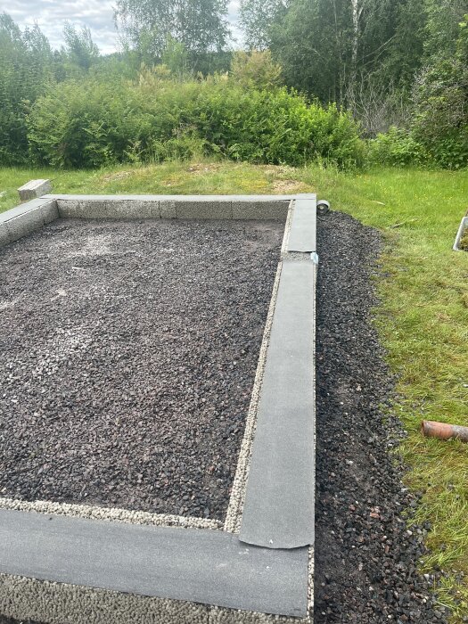 Grundarbete för byggprojekt med marksten och grus, omgärdat av grönska.