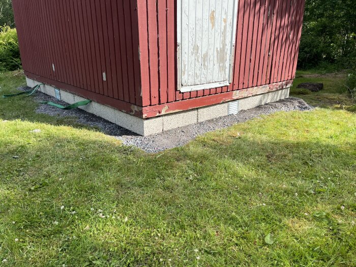 Röd fasad på ett hus med ny grusad grund och grön gräsmatta runt om.