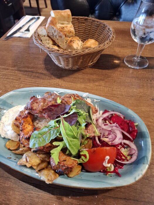 Portion med grillat kött, ris, potatis och sallad från arabisk restaurang, serverad med brödkorg och dryck på ett bord.