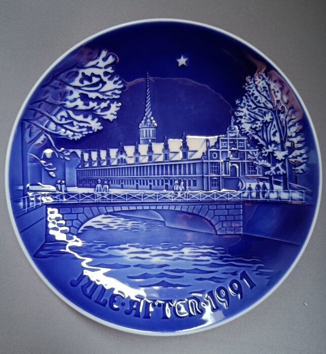 Blå jultallrik från 1991 med ett detaljrikt motiv av ett slott och en bro, träd och en stjärna i bakgrunden.