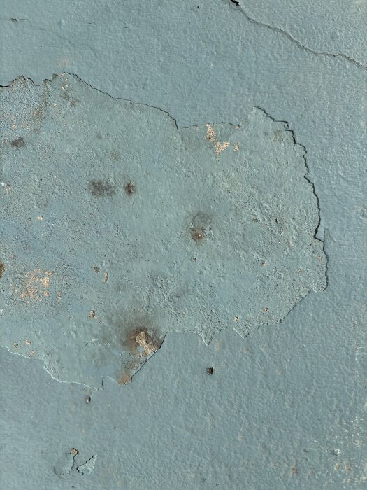 Avskavd blå färg på betongyta med fläckvis avskalning och synlig struktur.