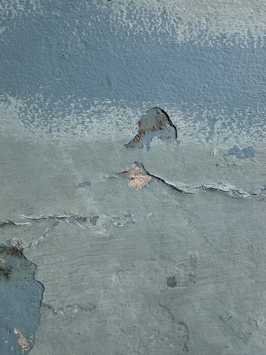 Flagnande blå färg på en altan med synliga sprickor och avskalad yta.