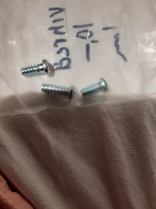 Tre skruvar med rund huvud på en plastpåse med handskriven text, avsedda för Elfa glidskena, storlek 1,5 cm lång och 5 mm diameter.