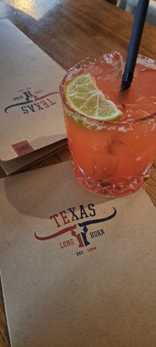 Drink med limeklyfta och svart sugrör på bordet vid Texas Longhorn, restaurangmeny synlig i bakgrunden.