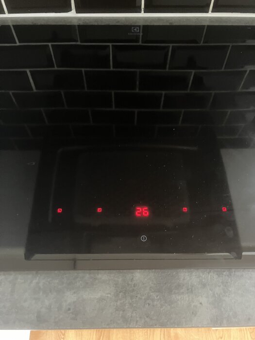 Induktionshäll från Electrolux med siffran 26 synlig på displayen, omgiven av fyra röda indikatorlampor, mot en svart kakelvägg.